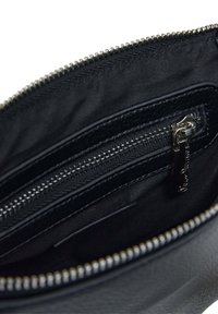 Unutrašnjost crne kožne torbe sa zip zatvaračem, srebrnim detaljima i glatkom teksturom. Sadrži više džepova i zatvarača.