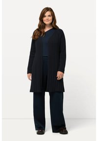 Lång, mörk marinblå kashmirtröja med ribbad textur, öppen fram, och långa ärmar, bärs över en matchande topp och löst sittande byxor.