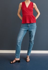 Czerwona bluzka z peplum, o fakturowanej tkaninie. Połączona z jasnoniebieskimi dżinsami o prostym kroju. Czarne sandały na obcasie dopełniają całość.