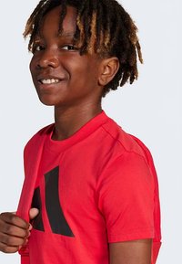 Κόκκινο βαμβακερό t-shirt με στρογγυλή λαιμόκοψη και κοντά μανίκια, με μεγάλο μαύρο σχέδιο λογότυπου στο μπροστινό μέρος και λεία υφή.