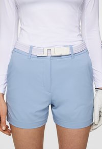 Ljusblå golfshorts i slätt tyg, med ett vitt flätat bälte med en glänsande spänne och sidfickor.