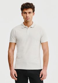Jasno-beżowa koszulka polo wykonana z miękkiej bawełny, z klasycznym kołnierzykiem, krótkimi rękawami oraz subtelnym logo haftowanym na lewej piersi.