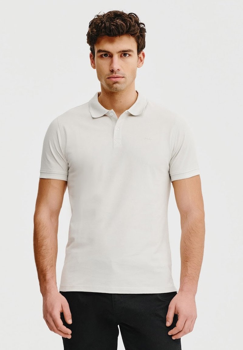 Jasno-beżowa koszulka polo wykonana z miękkiej bawełny, z klasycznym kołnierzykiem, krótkimi rękawami oraz subtelnym logo haftowanym na lewej piersi.