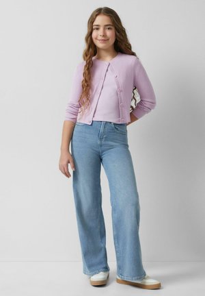 Helllila gerippter Cardigan mit Knopfdetails über einem helllila Top, kombiniert mit hellblauen weit geschnittenen Jeans und weißen Sneakers.