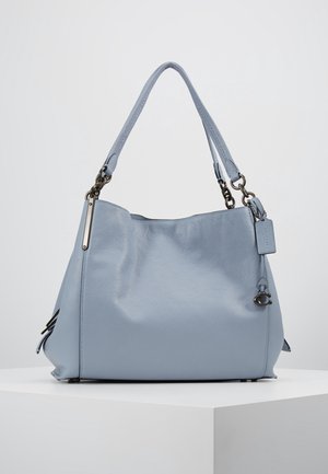Jasnoniebieska skórzana torebka z dwoma paskami na ramię, metalowymi okuciami i małą zawieszką z logo z boku, prezentowana na białej powierzchni.