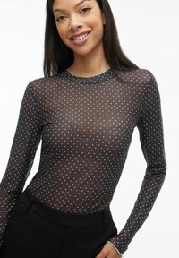 Czarny top z siateczki z długim rękawem i okrągłym dekoltem, w czarne groszki, z przezroczystą teksturą, nałożony na czarną bazową warstwę.