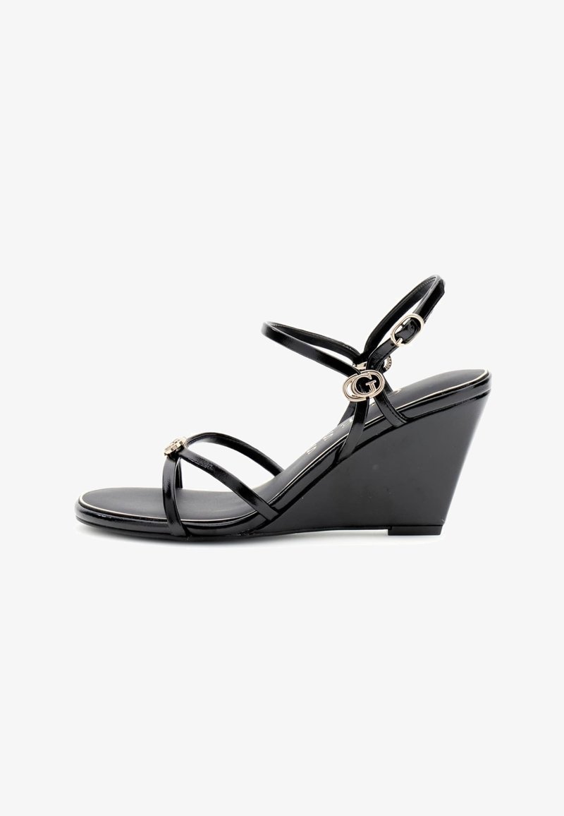 Sandale compensée noire avec des fines brides et une petite boucle dorée sur les brides de la cheville et des orteils.