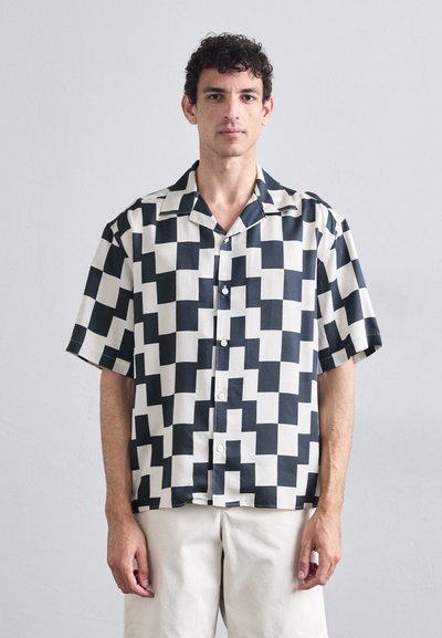 Chemise à manches courtes avec des boutons, arborant un motif géométrique audacieux en noir et blanc, fabriquée à partir d'un tissu lisse avec une coupe décontractée.