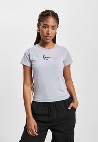 T-shirt in cotone grigio con maniche corte, dotato di un logo nero in stile scritto a mano sul davanti e un collo rotondo.