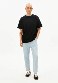 Zwart katoenen T-shirt met ronde hals, losse pasvorm; gecombineerd met lichtblauwe jeans met rechte pijpen en zwarte sneakers met witte veters.