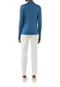Langarmige blauwe top met hoge kraag en zijsplitten, gecombineerd met witte slim-fit broek en witte sneakers met zilveren accenten.