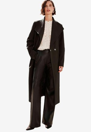 Black wool blend coat with a wide collar, double-breasted closure, and long sleeves; paired with black high-waisted leather trousers.