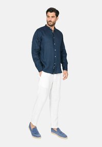Camicia di lino blu navy con colletto alla cinese, pantaloni di lino bianchi e espadrillas in suede blu. Chiusura con bottoni semplice e vestibilità rilassata.