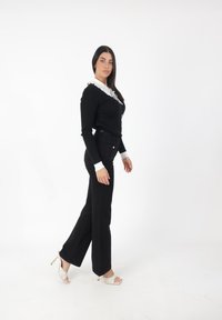 Suéter negro de canalé con cuello blanco con volantes, combinado con jeans negros de tiro alto y zapatos de tacón abiertos beige. Diseño liso y ajustado.