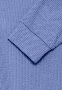 Manche de pull tricotée violet clair avec poignets côtelés et motif vertical texturé s'étendant sur toute la surface du tissu.