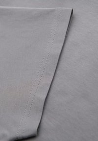 Tejido gris con una textura suave, que presenta un borde limpio y una costura estrecha y recta a lo largo del dobladillo. Color sutil y uniforme.
