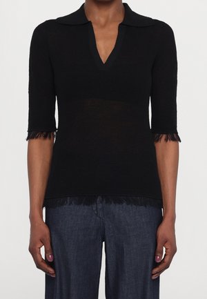 Czarny top z krótkim rękawem, kołnierzykiem i frędzlami na krawędziach, noszony z ciemnoniebieskimi dżinsami, widoczny od szyi do bioder.