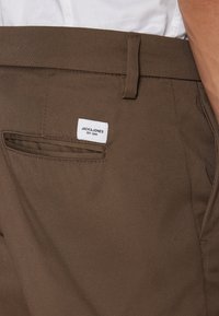 Brown cotton trousers featuring a label with "JACK & JONES EST. 1990," a back pocket, and a smooth textured surface.