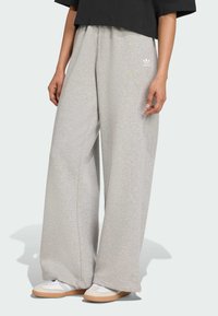 Sive široke trenirke od mekog materijala, s malim bijelim Adidas logom. Uparene s bijelim sportskim cipelama i crnim skraćenim topom.