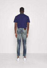 Granatowa koszulka, wyblakłe niebieskie dżinsy i białe trampki. Dżinsy mają slim fit i kontrastową brązową skórzaną metkę z tyłu.