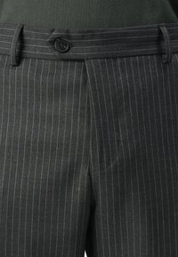 Dark gray pinstripe trousers with a black button and belt loops, worn with a tucked-in dark green top.