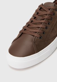 Barna sneaker, sima bőrből készült orral és velúr felsőrésszel. Kerek formájú, fűzős kialakítású, fehér gumitalppal, amely textúrázott díszítésekkel rendelkezik.