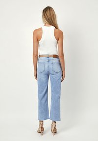 Witte geribbelde tanktop gecombineerd met lichtblauwe high-waisted rechte jeans, voorzien van een bruine riem en beige haksandalen.