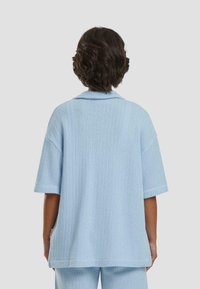 Light blue knit short-sleeve top with a relaxed fit, ribbed texture, and a small collar, featuring side slits and rolled cuffs.