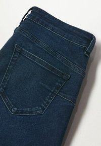 Tmavě modré denimové džíny s hladkým povrchem, s jednou zadní kapsou a poutky na opasek. Tkanina má jemný vzor tkaní.