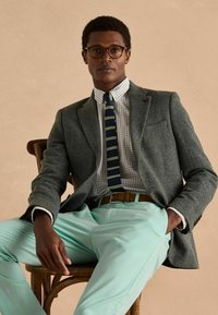 Szürke halszálka mintás blézer fehér, zöld csíkos kockás inggel, barna övvel és mentazöld nadrággal. A szemüveg fokozza a megjelenést.