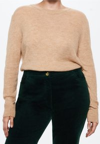 Vaaleanbeige neulepaita pitkillä hihoilla ja pyöreällä kaula-aukolla, yhdistetty tummanvihreisiin kordidikkihousuihin, joissa on nappisulku ja sivutaskut.