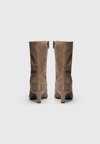 Bottines en suède marron avec un talon légèrement effilé, dotées d'une fermeture éclair à l'arrière et de détails de couture subtils sur les côtés.