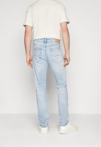 Ljusblå jeans i slim fit, med två bakfickor och en tanfärgad läderlapp vid midjan. Materialet visar lätt blekning.