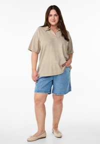 Polo beige a maniche corte, abbinato a pantaloni corti in denim blu. Il modello indossa ballerine neutre. Design semplice, vestibilità rilassata.