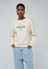 Světlý krémový svetr s potiskem "SALSA jeans" v černé barvě, se zlatými knoflíky na levém rameni a žebrovanými manžetami.