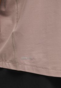 Rožinė sportinė palaidinė su tekstūruotu audiniu. Ant jo yra užrašas „COOLCELL“. Lygūs siūlės ir hem juodos spalvos drabužio viršuje. Lengvas medžiagos svoris.