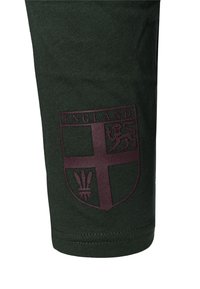 Tmavě zelený bavlněný oděv s bordó štítovým motivem, na kterém je nápis „ENGLAND“ a emblém lva. Hladká textura.