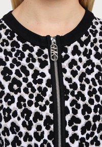 Veste à motif léopard noir et blanc avec col côtelé et fermeture éclair argentée. Présente un tissu en tricot texturé avec des accents contrastants.