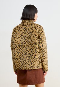 Kabát z umělé kožešiny s leopardím vzorem, s límcem, s boxy střihem, černými skvrnami na béžovém pozadí a žebrovaným lemem.