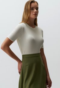 Biała dopasowana bluzka z prążkowanego materiału, z falbaniastym dekoltem i krótkimi rękawami, połączona z zieloną spódnicą o wysokim stanie, eksponującą gładkie faktury.