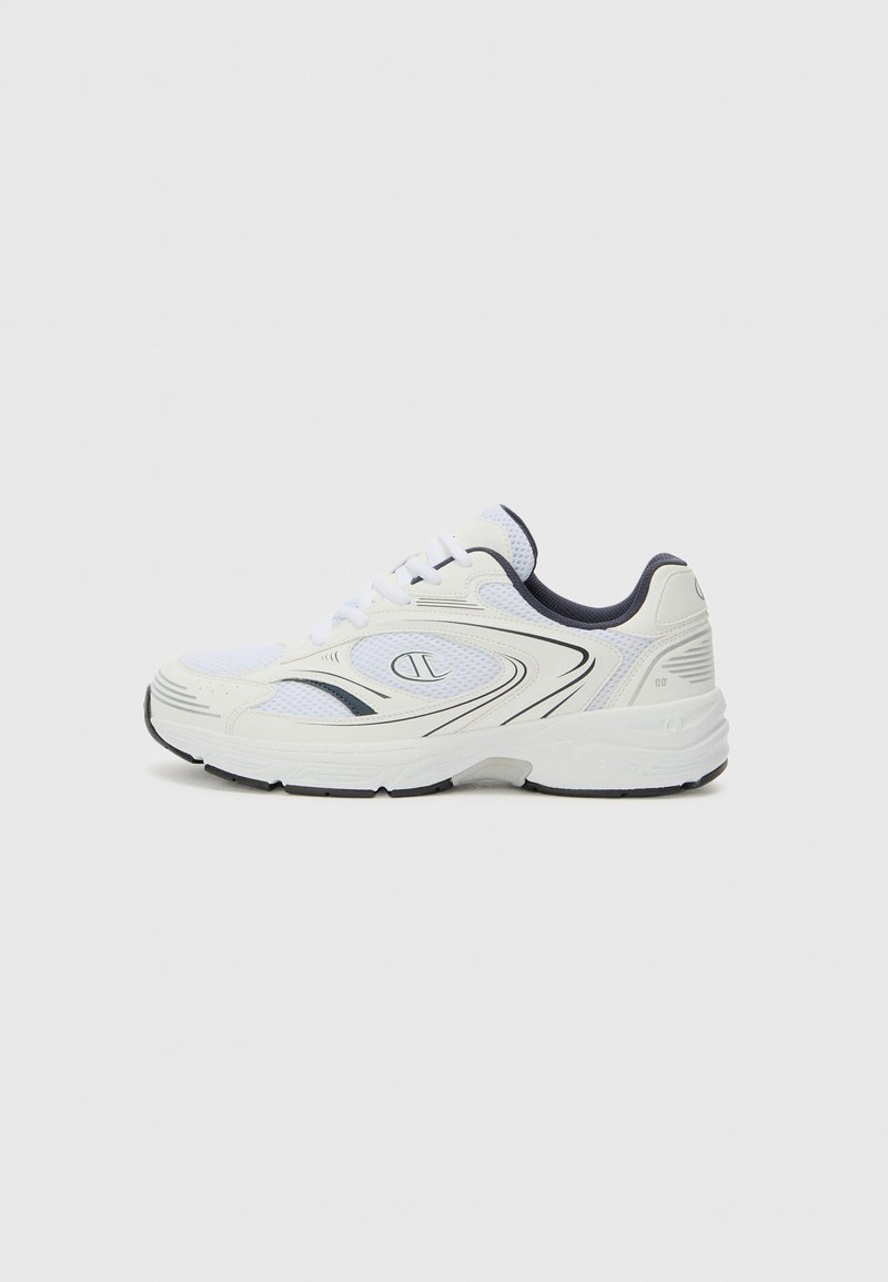 Zapatilla deportiva blanca con detalles de malla, acentos negros, suela acolchada y curvas suaves. Presenta un logo en el lateral y una suela de goma negra.