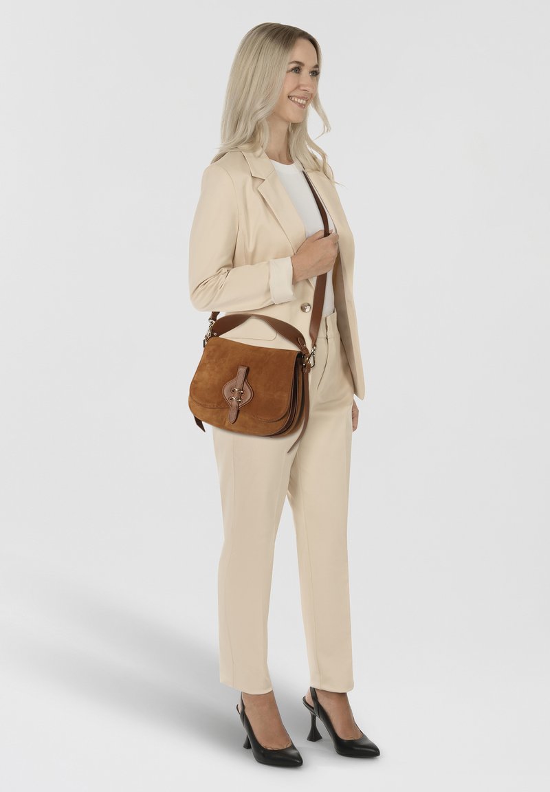 Bruine suède crossbody tas met leren accenten en een decoratieve gesp, voorzien van een comfortabele schouderriem. Eenvoudig, rechthoekig ontwerp.