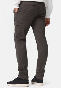 Cargo byxor i mörkgrått, tillverkade av ett slätt tyg. Har sidofickor och en åtsittande design. Bärs med svarta sneakers.