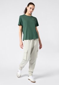 Grünes Baumwoll-T-Shirt mit rundem Ausschnitt und kurzen Ärmeln, kombiniert mit hellgrauen Cargo-Hosen, die große Taschen und umgeschlagene Knöchel haben.