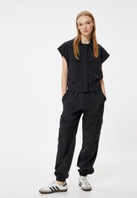 Zwarte cropped shirt met korte mouwen, twee borstzakken; bijpassende zwarte cargobroek met elastische boorden; gecombineerd met witte sneakers.
