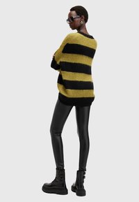 Maglione oversize a maglia con righe gialle e nere, abbinato a leggings neri lucidi e stivali neri spessi.