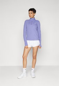 Svijetloplavi dugi rukav s polu-zip ovratnikom, u kombinaciji s bijelim sportskim kratkim hlačama i cipelama, stvara sportski izgled.