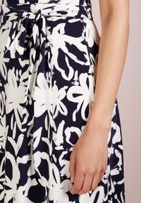 Abito stampato floreale in blu navy e bianco, realizzato in tessuto morbido. Presenta un dettaglio in vita annodato e motivi floreali di grandi dimensioni in colori a contrasto.