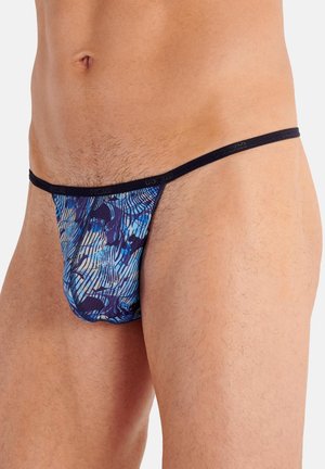 Männlicher Oberkörper trägt einen blau gemusterten, tief sitzenden Tanga mit dünnem schwarzem elastischem Bund vor weißem Hintergrund.