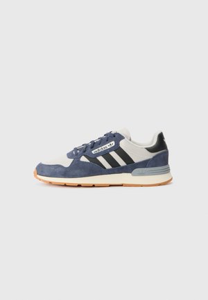 Baskets en daim navy et textile gris avec des rayures noires, un logo blanc et une semelle en caoutchouc beige. Présente des lacets ronds et un col rembourré.